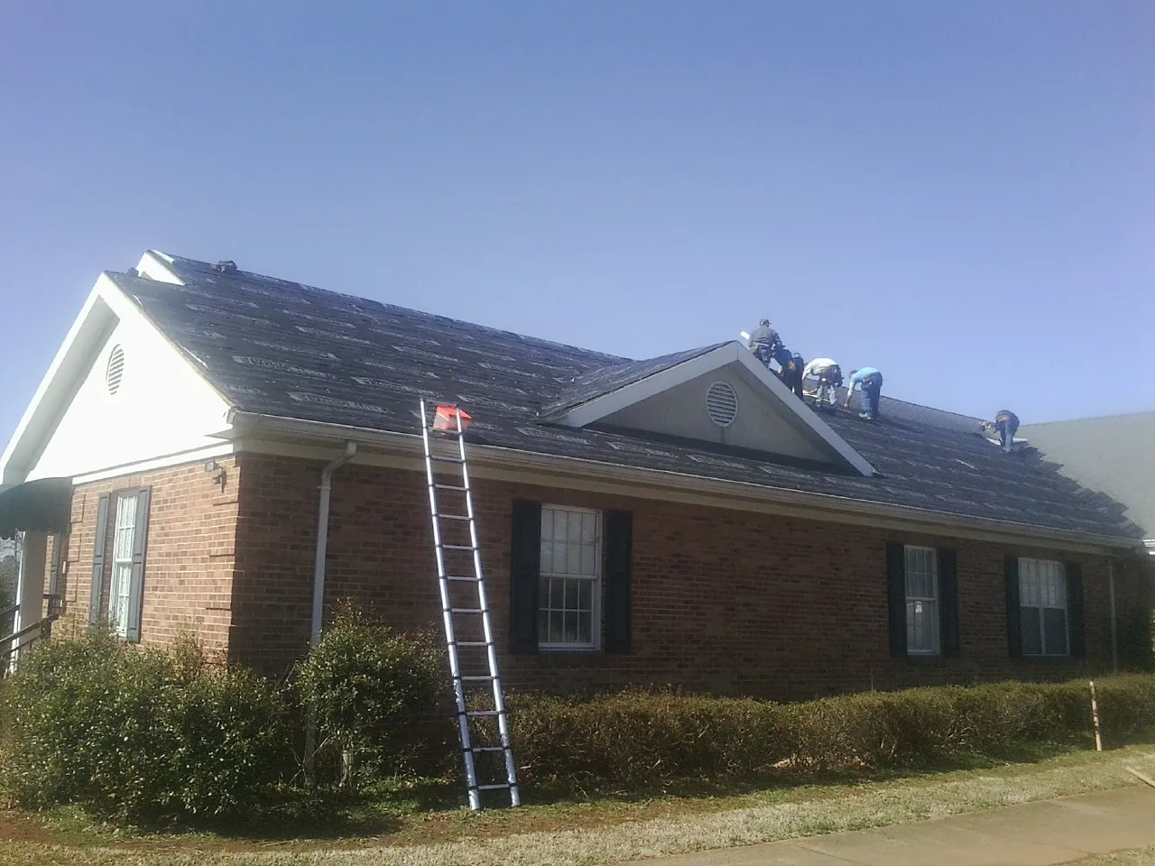 Crew tearing shingles off a brick ranch roof with a ladder set — Metal Roof Repair work by our crew in Grahamsville