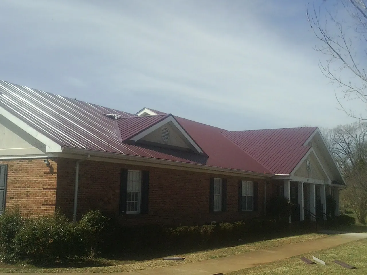 Red metal roof with gabled entries on a long brick building, from a Hail Damage Roof Repair job in Grahamsville