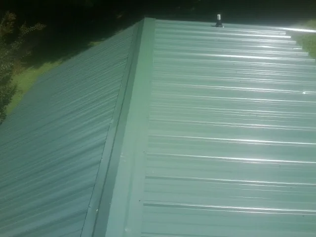 New green metal panels meeting at the ridge of a roof — Flat Roof Repair work by our crew in Grahamsville