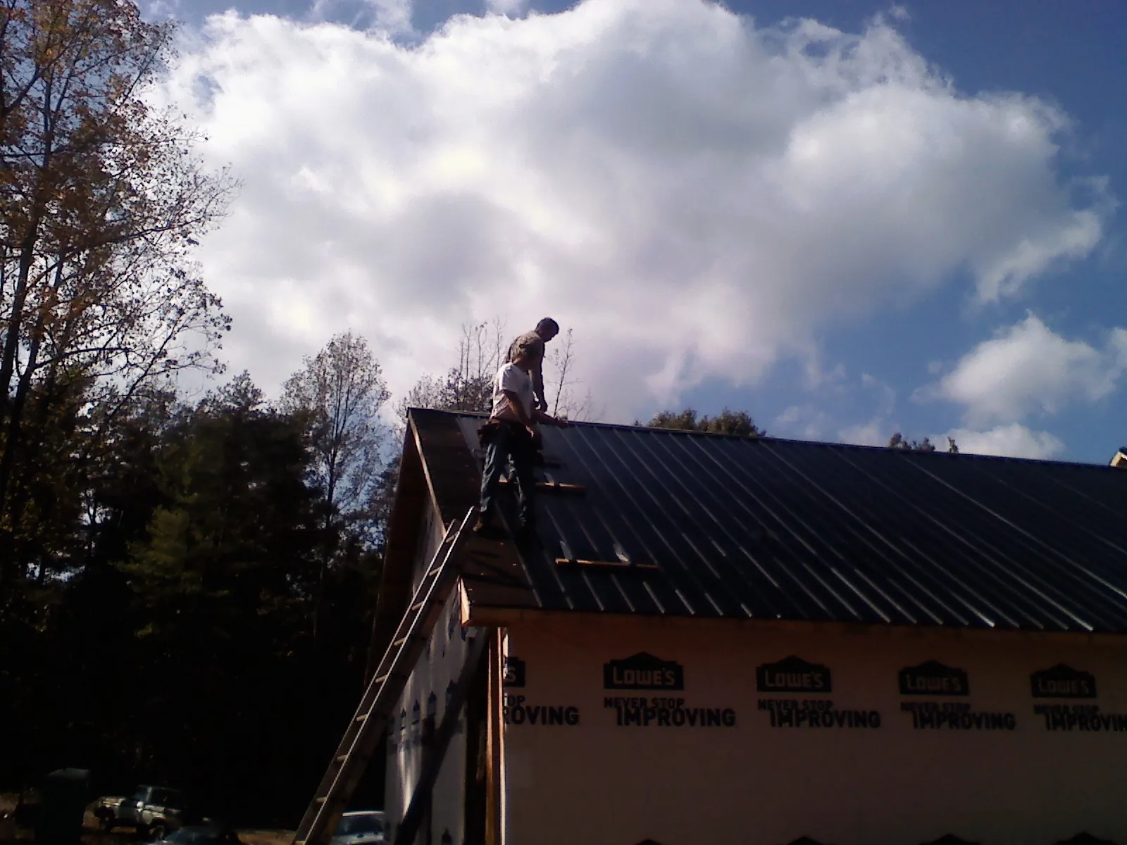Roofer fastening dark metal panels high against a cloudy sky, from a Roof Inspection job in Grahamsville