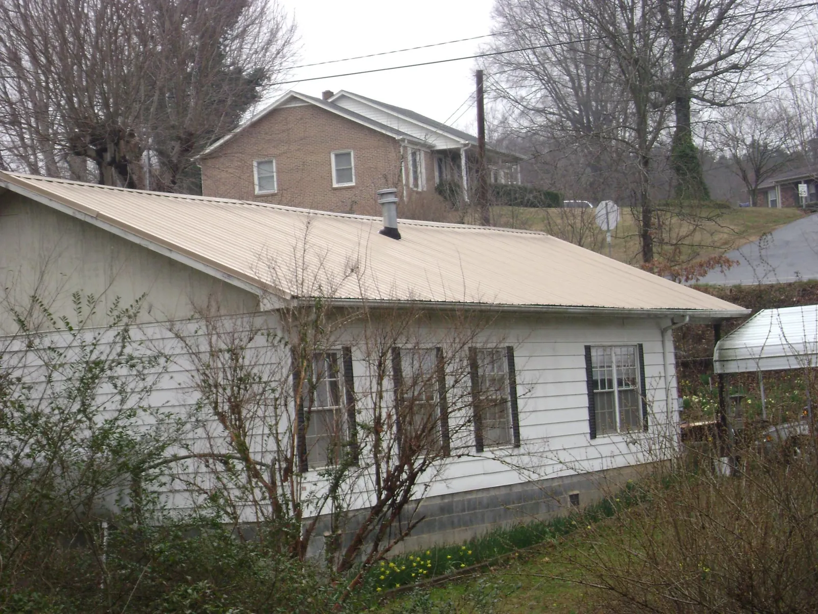 Tan metal roof on a white sided house set into a hillside — Commercial Roofing by Roofing Brothers in Grahamsville